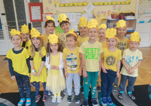 rupa dzieci przedszkolnych znajdujących się w klasie w żółtych strojach i opaskach z emblematem słońca uśmiecha się okazując radość i zadowolenie w dniu ich święta - Dnia Przedszkolaka.